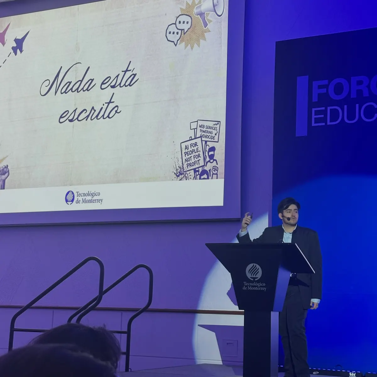Alberto Gallegos junto al podio durante la conferencia, con la diapositiva “Nada está escrito” proyectada