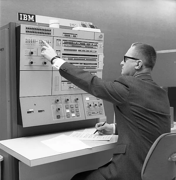 Hombre con lentes señalando el panel de control de una computadora IBM de mainframe